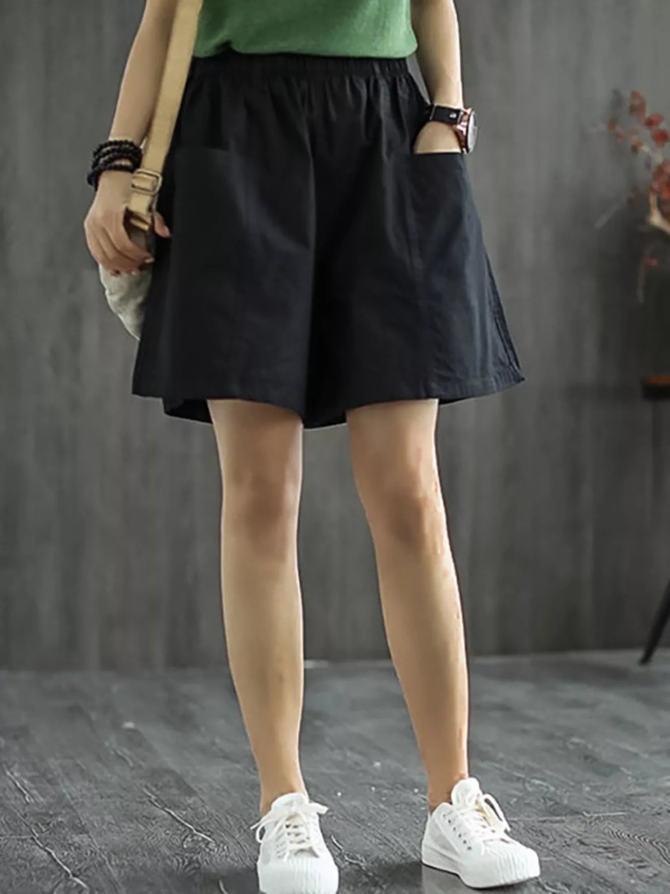 Person wearing black shorts and white sneakers on a gray background