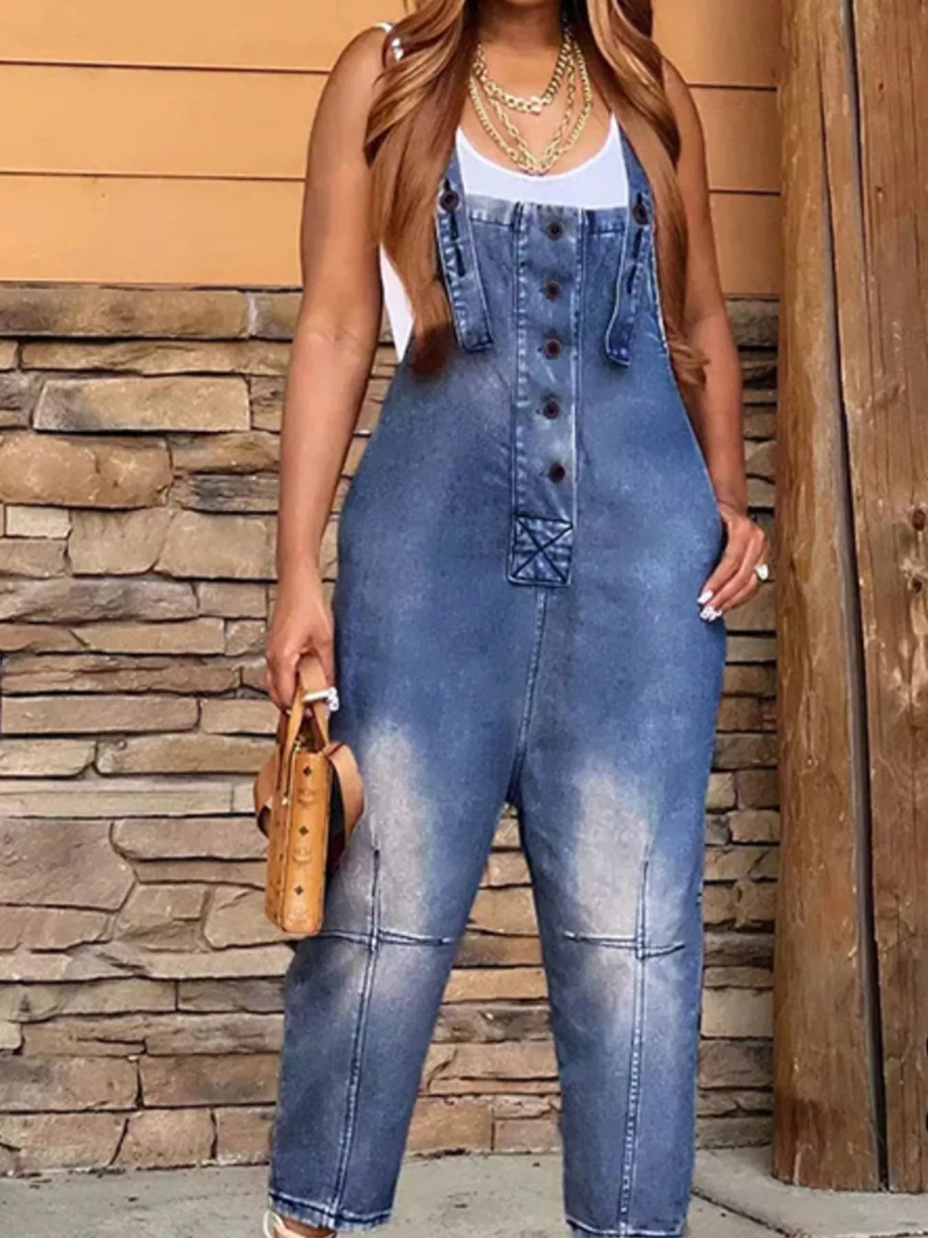 Person wearing a blue denim jumpsuit against a stone wall background