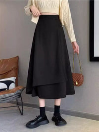 Person wearing a black skirt with a beige sweater and black shoes in an indoor setting.