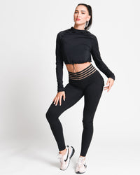 Woman wearing a black long-sleeve top and black leggings with gold accents on a white background