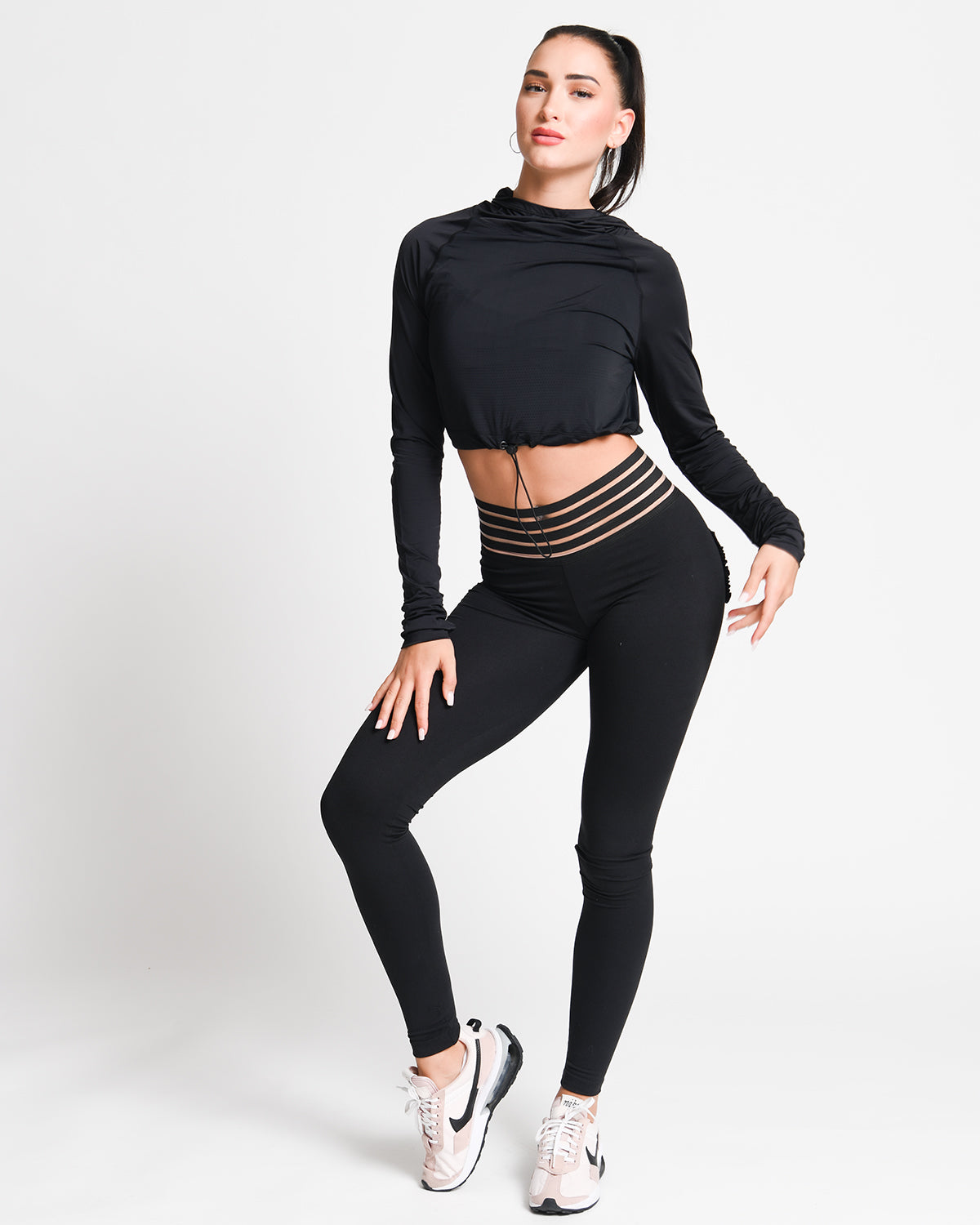 Woman wearing a black long-sleeve top and black leggings with gold accents on a white background