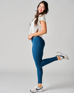 Woman wearing blue leggings and a white top on a gray background