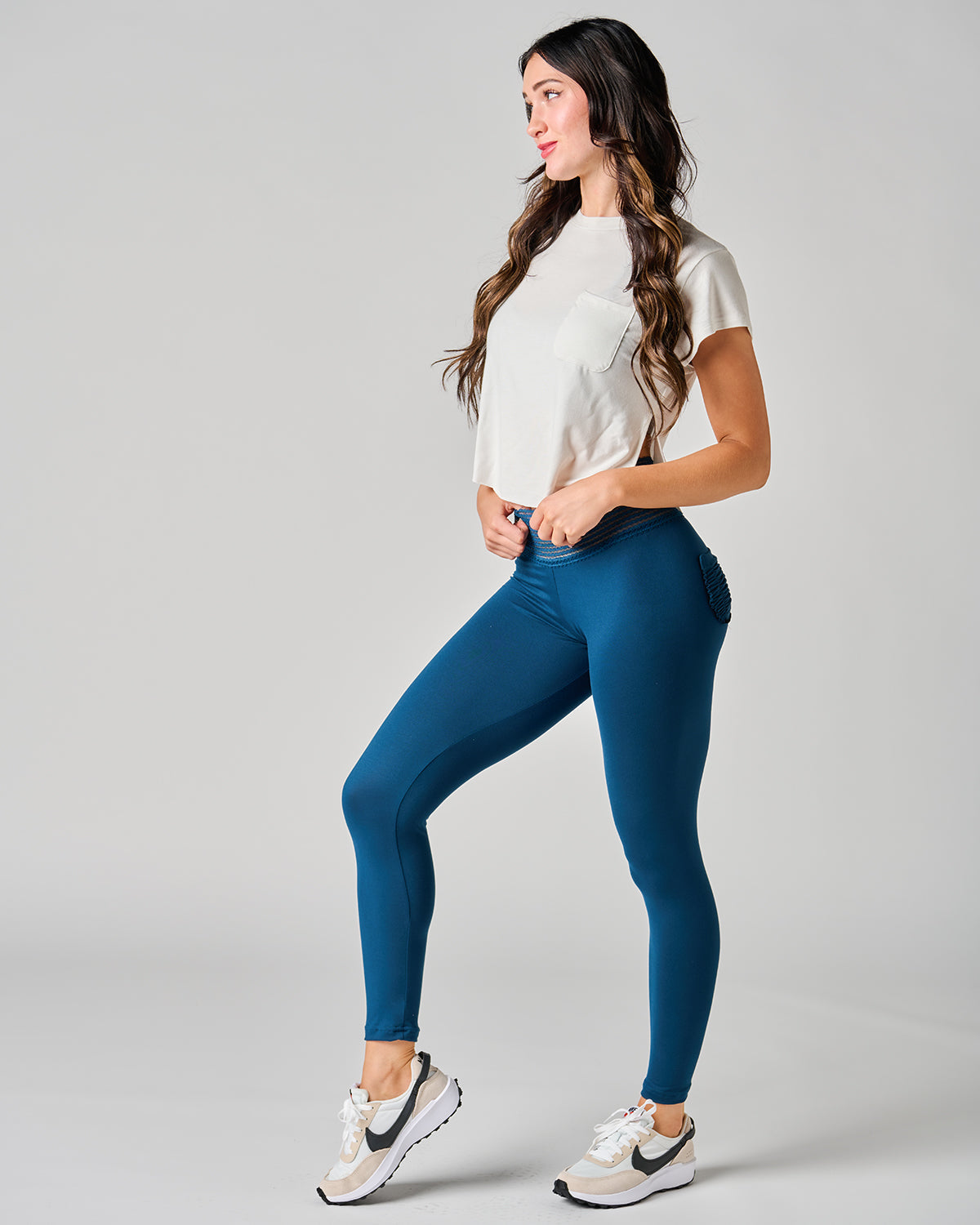 Woman wearing blue leggings and a white top on a gray background