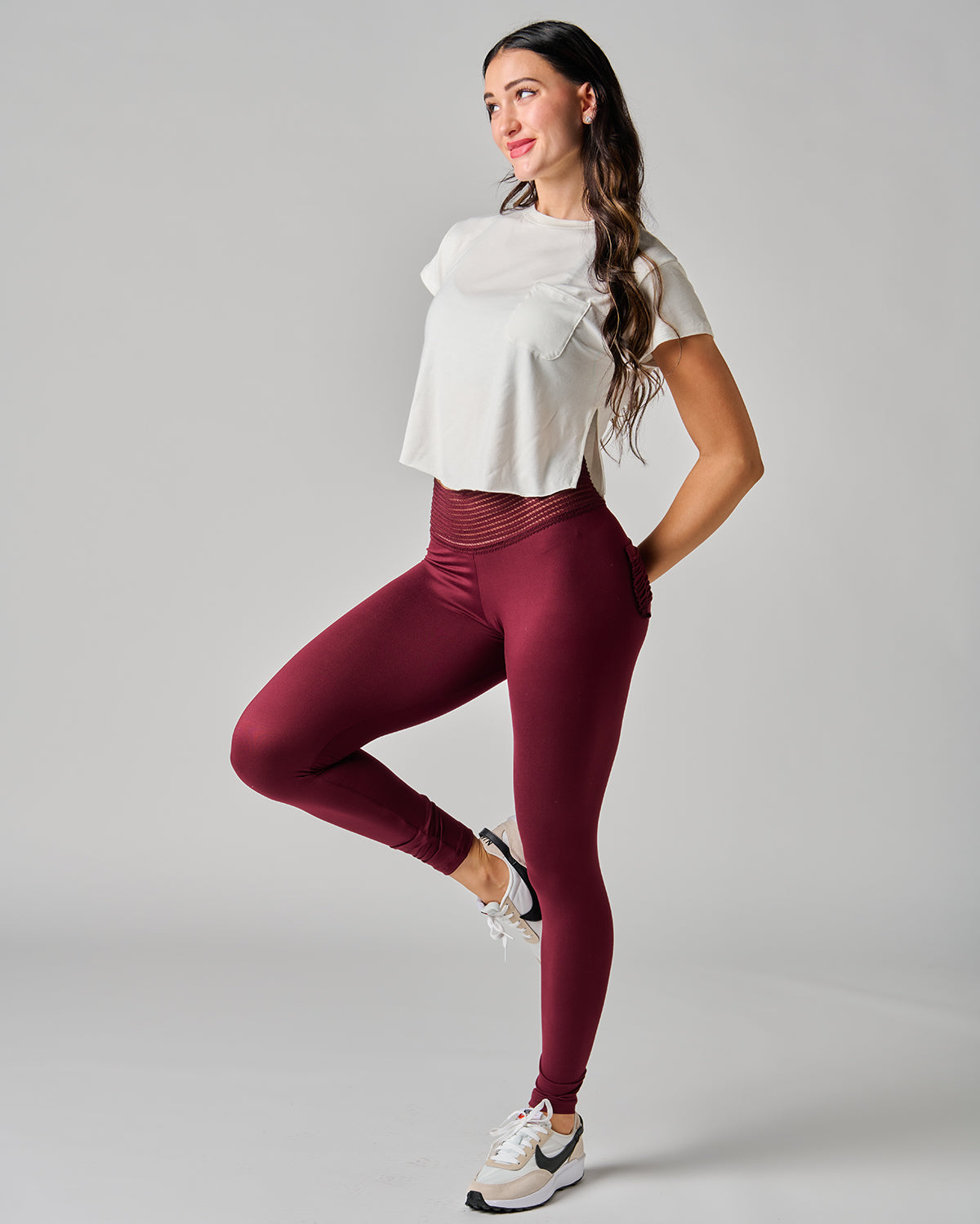 Woman wearing a white top and maroon leggings on a gray background