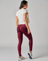 Woman wearing maroon leggings and a white crop top on a gray background