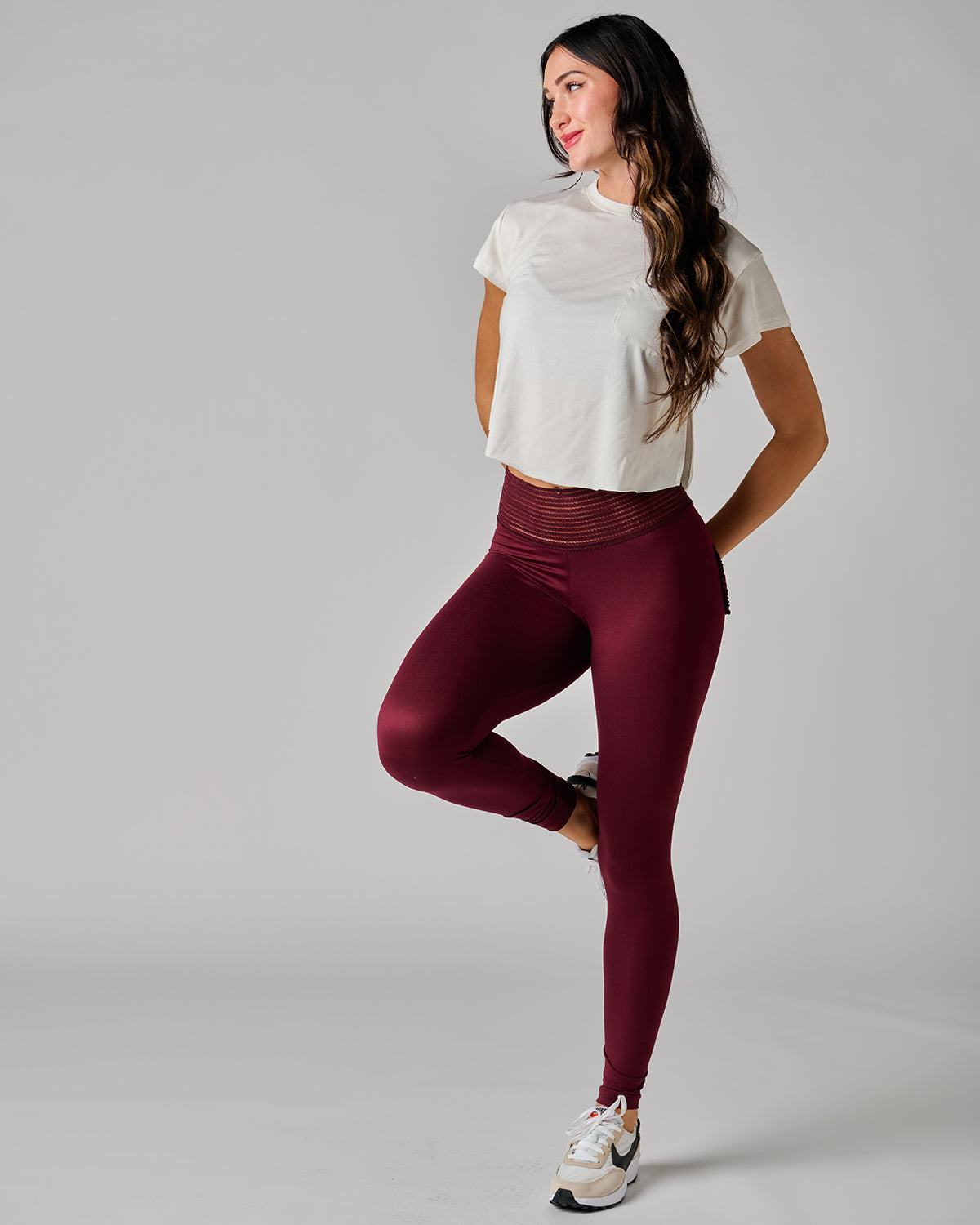 Woman wearing a white crop top and maroon leggings on a gray background