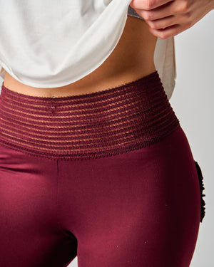 Maroon leggings with a textured waistband worn by a person on a light gray background