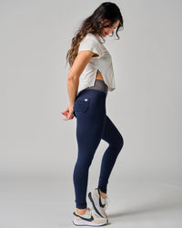 Woman wearing navy leggings and a white shirt on a gray background