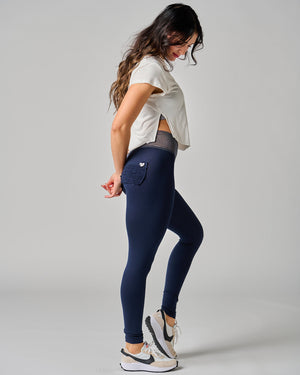 Woman wearing navy leggings and a white shirt on a gray background