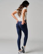 Woman wearing navy leggings and a white top on a gray background