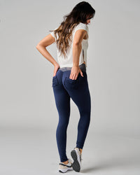 Woman wearing navy leggings and a white top on a gray background