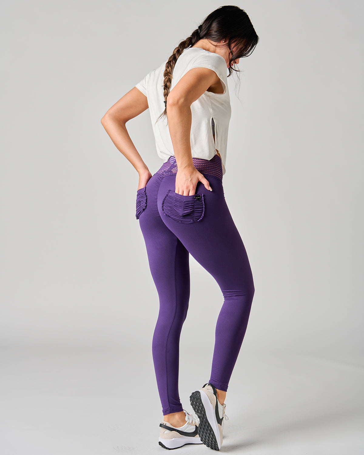 Woman wearing purple leggings and a white top on a gray background