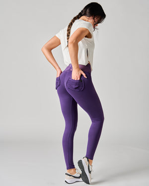 Woman wearing purple leggings and a white top on a gray background