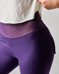 Purple leggings with a textured waistband worn by a person on a light gray background