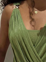 Close-up of a person wearing a draped olive green halter-style top or dress with a shimmering finish and a small gold heart pendant necklace.
