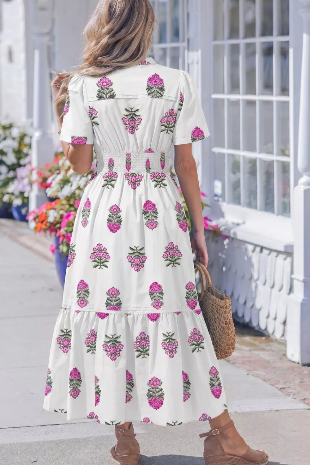 Woman wearing a white dress with pink floral patterns, standing on a porch.