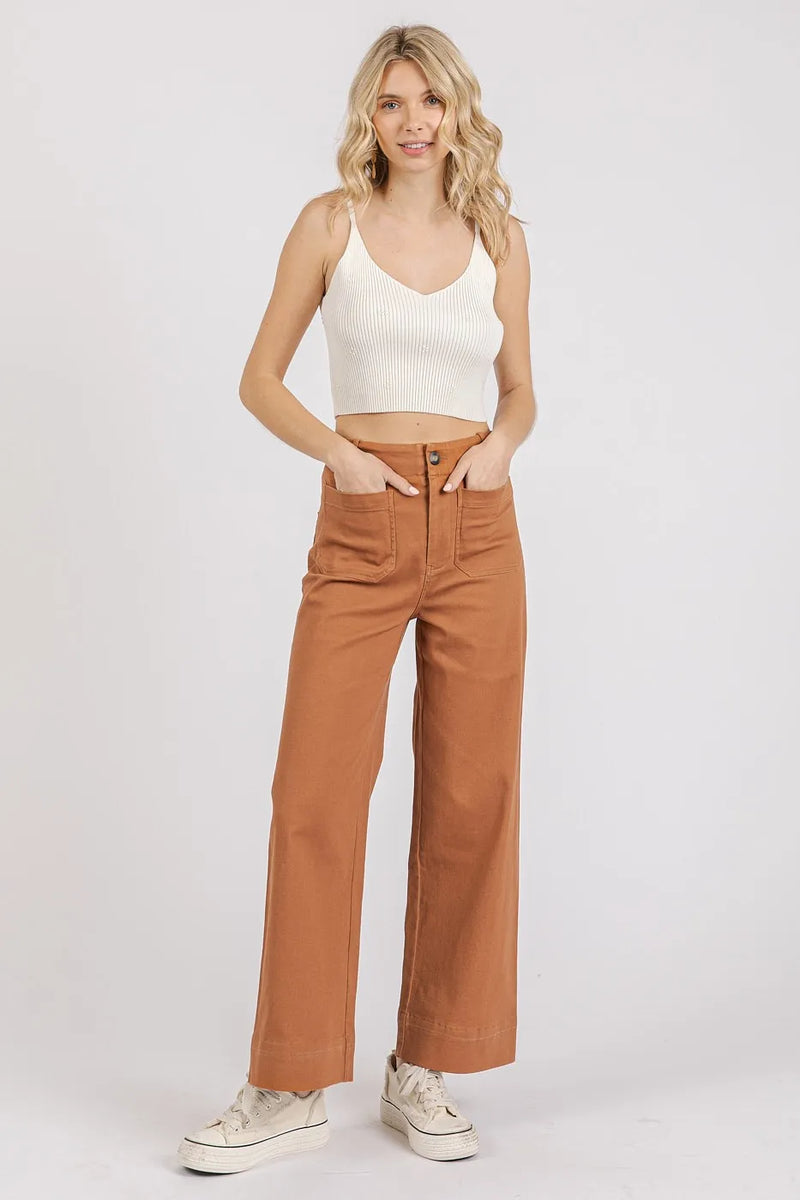 Woman wearing a white tank top and brown pants on a white background