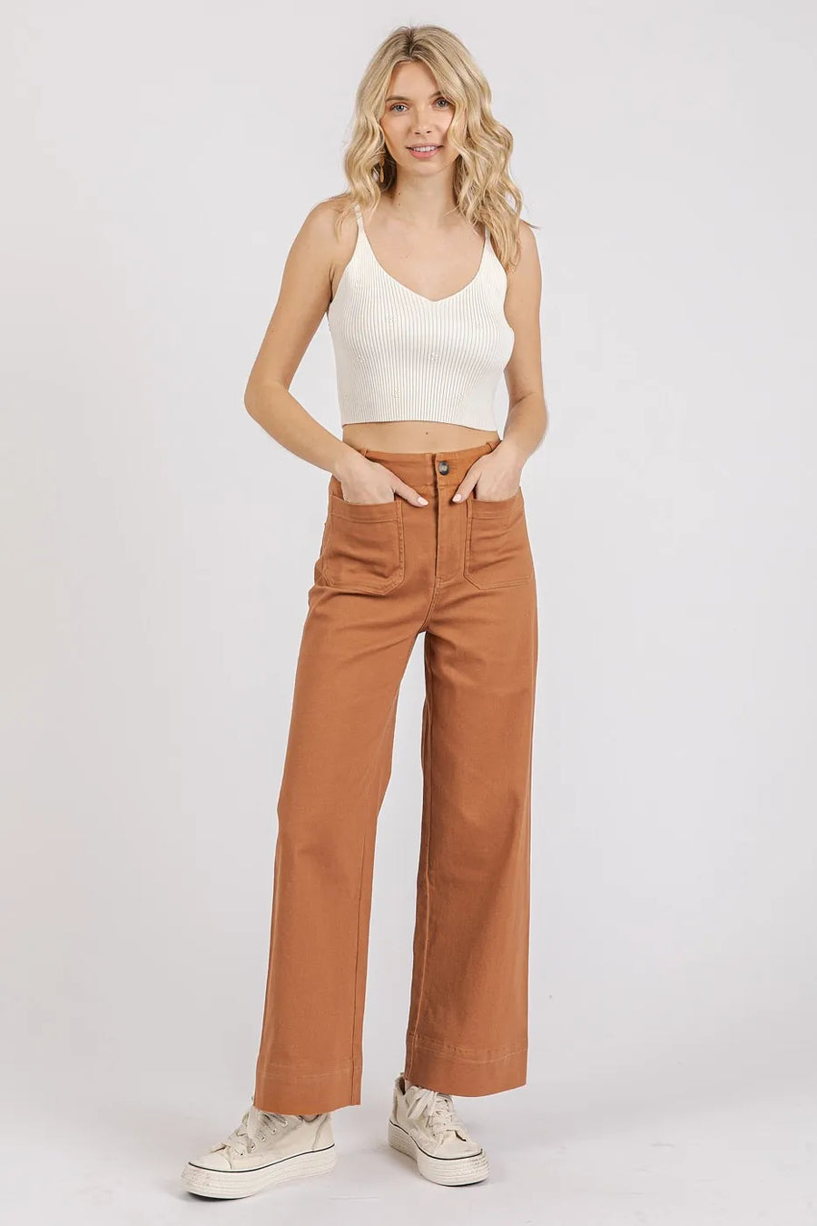 Woman wearing a white tank top and brown pants on a white background