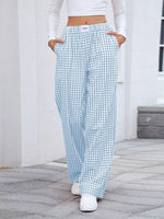 Person wearing light blue and white checkered pants with a white top, standing on a stone pavement.