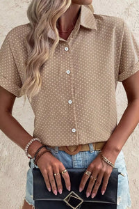 Woman wearing a beige polka dot shirt with denim shorts, holding a black clutch.
