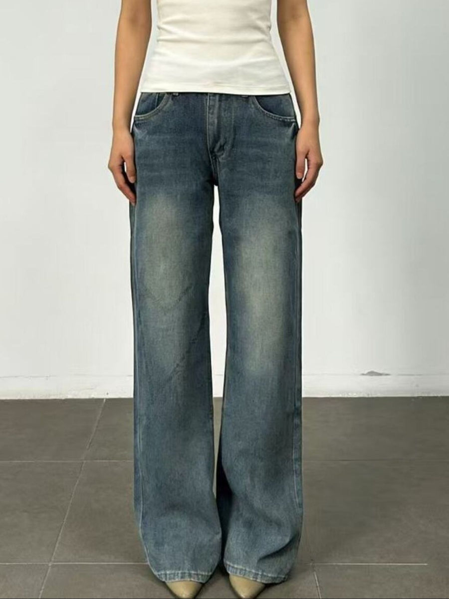 Person wearing blue wide-leg jeans and a white top on a plain background