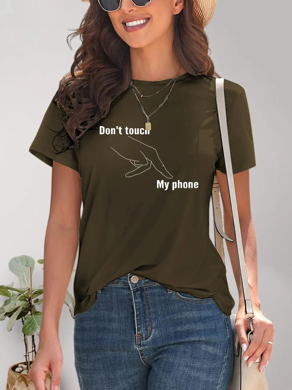 Woman wearing a green t-shirt with text and blue jeans, standing against a neutral background.