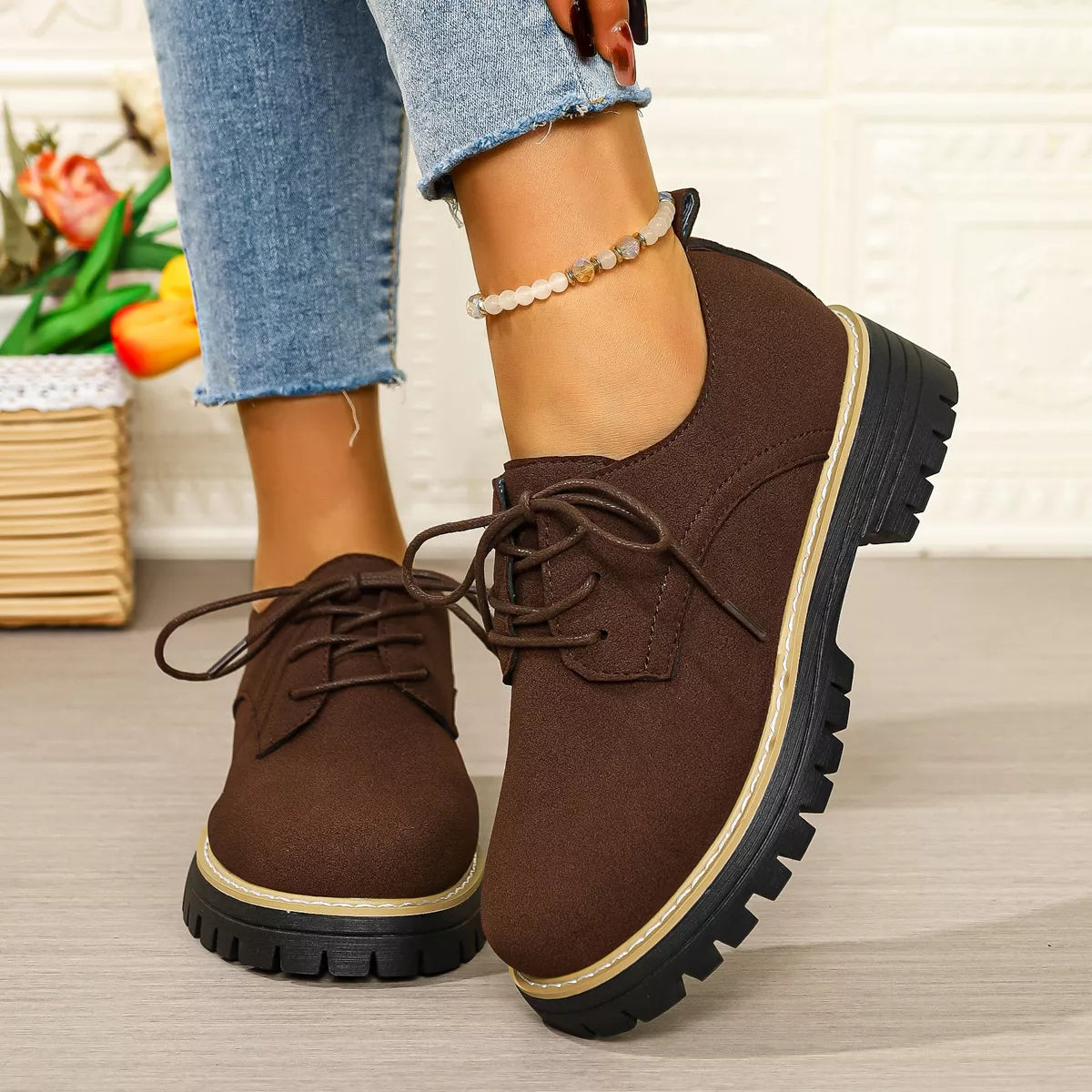 Brown lace-up shoes worn with blue jeans on a light wooden floor.