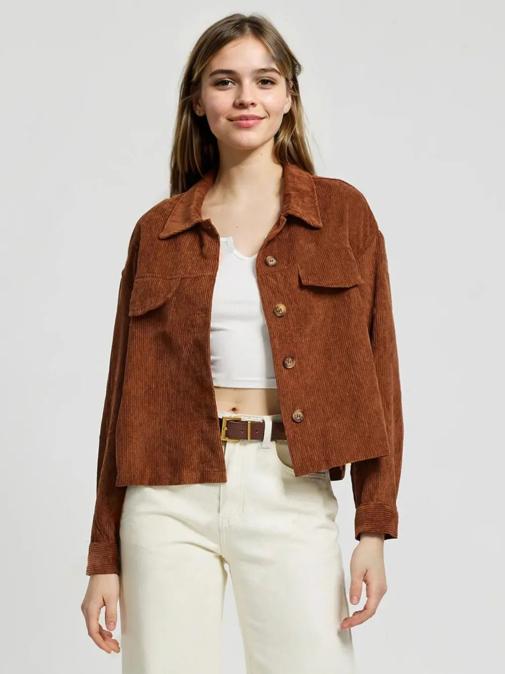 Woman wearing a brown jacket over a white top and beige pants on a plain background