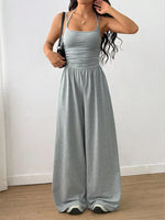 Woman wearing a gray jumpsuit against a white wall.