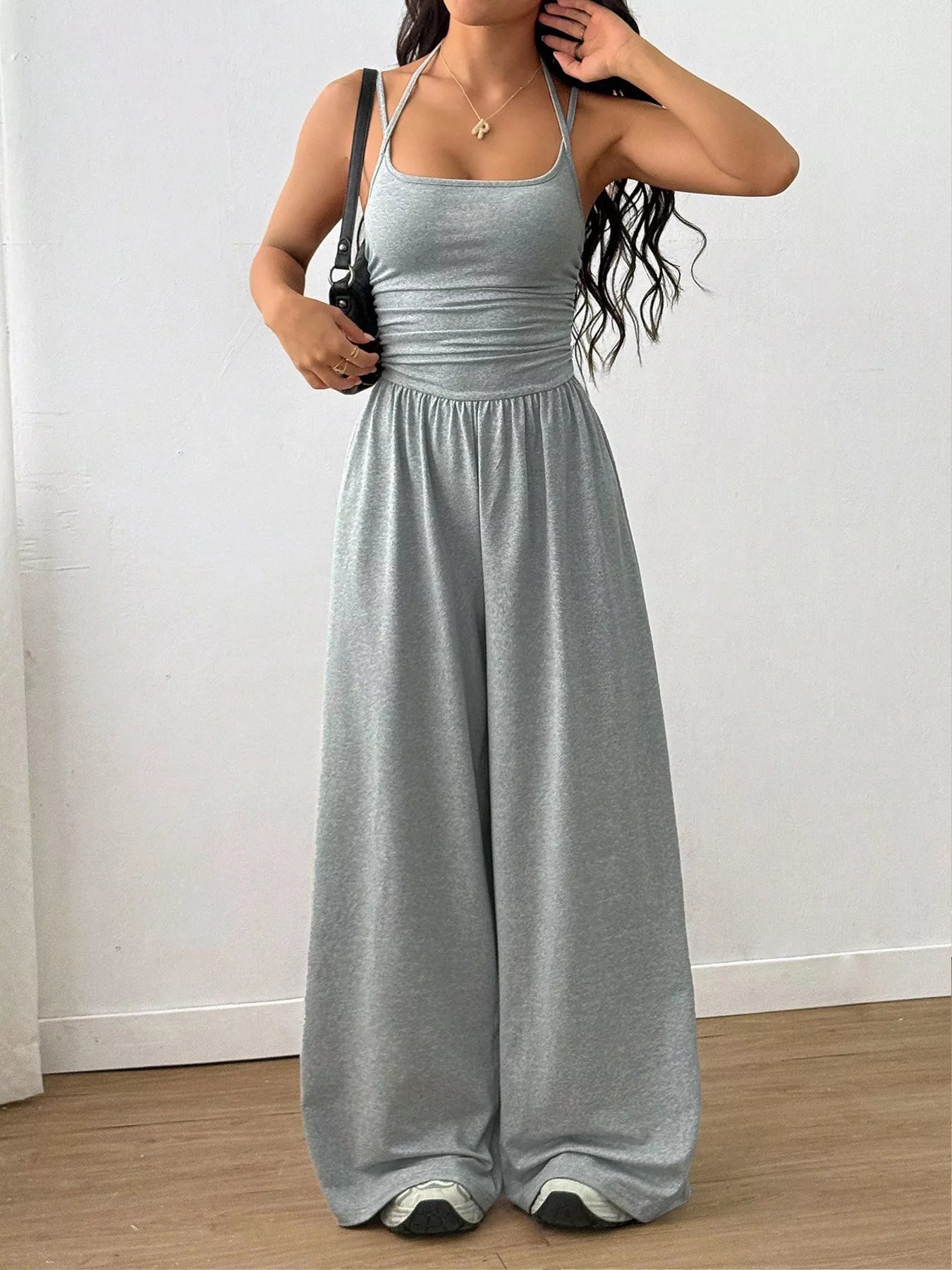 Woman wearing a gray jumpsuit against a white wall.