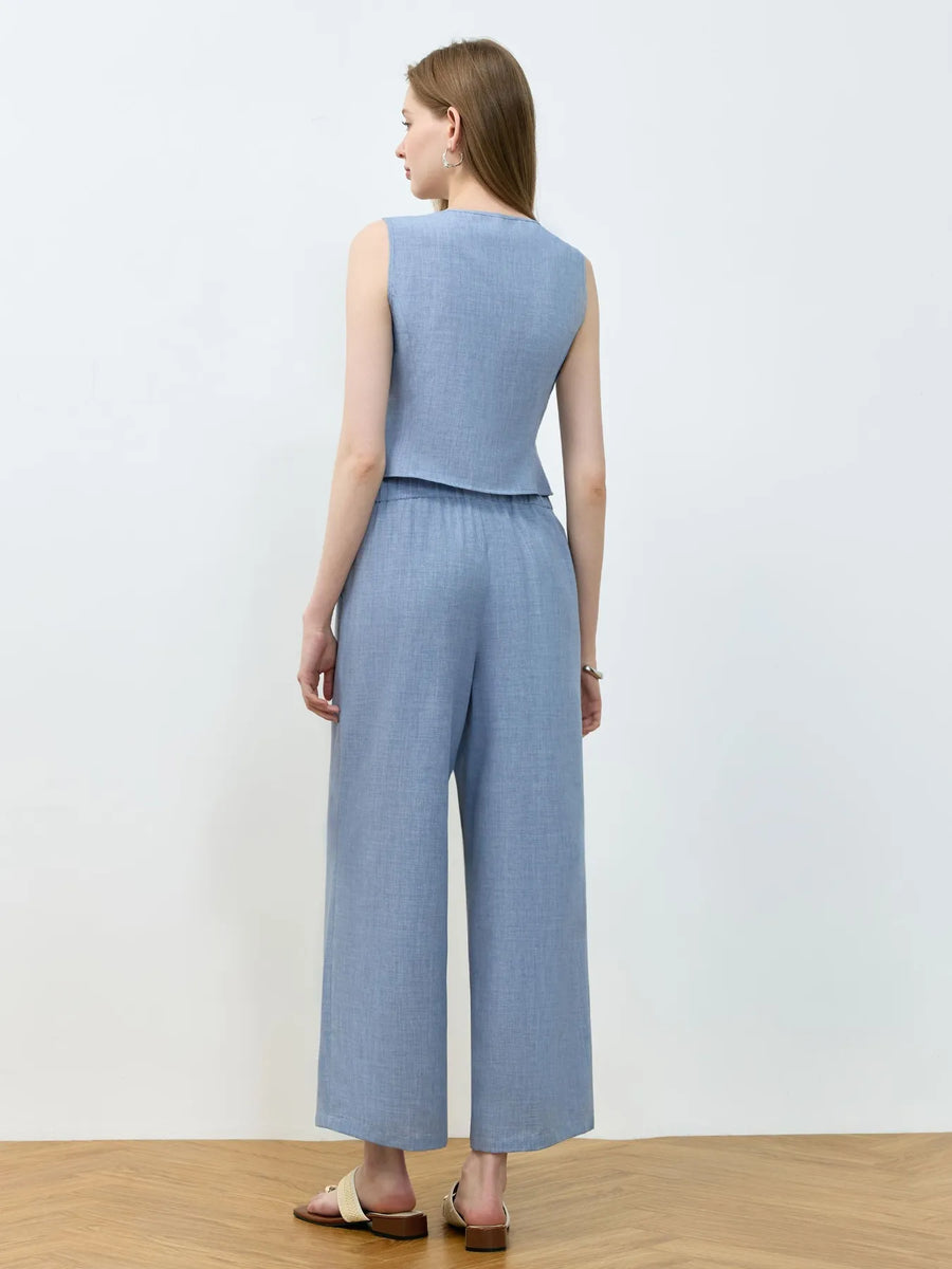 Woman wearing a light blue sleeveless top and wide-leg pants on a plain background
