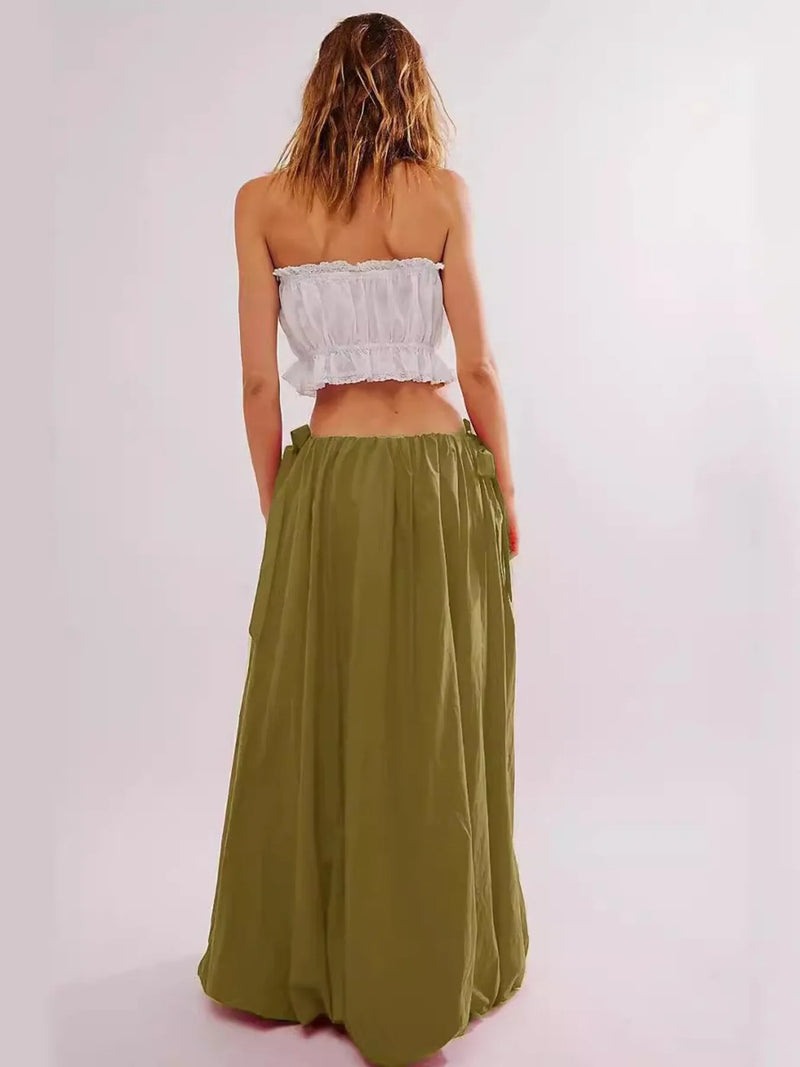 Woman wearing a white strapless top and green skirt on a light pink background