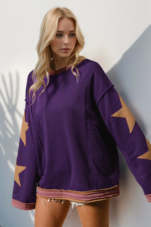 Woman wearing a purple sweater with star patterns against a white wall.