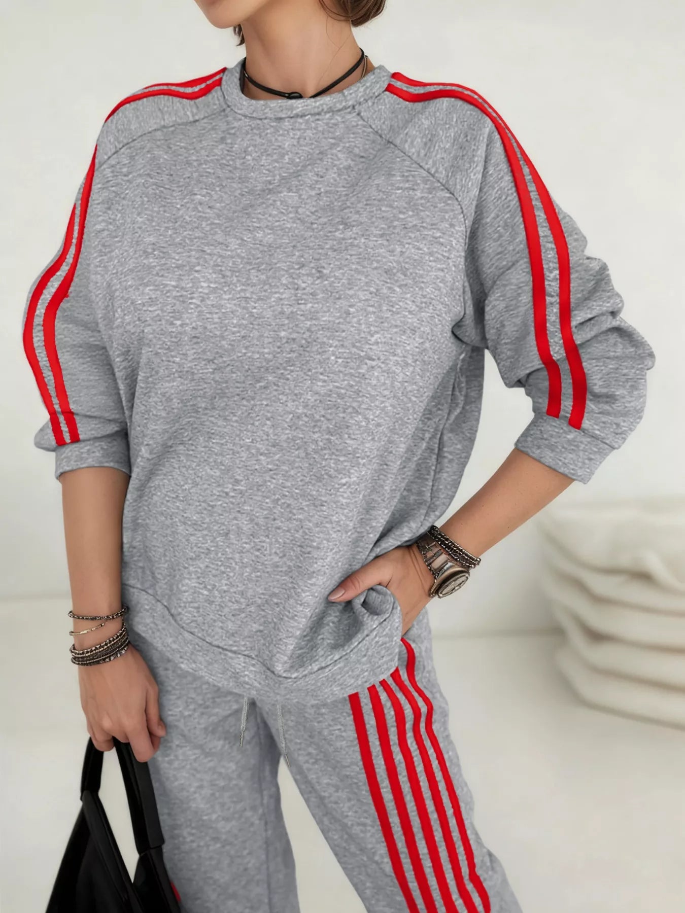Person wearing a gray tracksuit with red stripes on a plain background