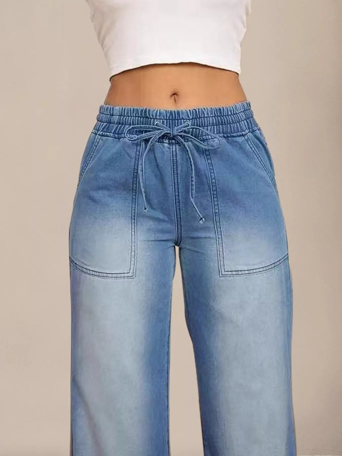 Light blue jeans with a drawstring waist on a beige background