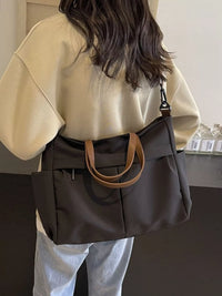 Person wearing a beige top and holding a dark brown handbag with a tan handle.