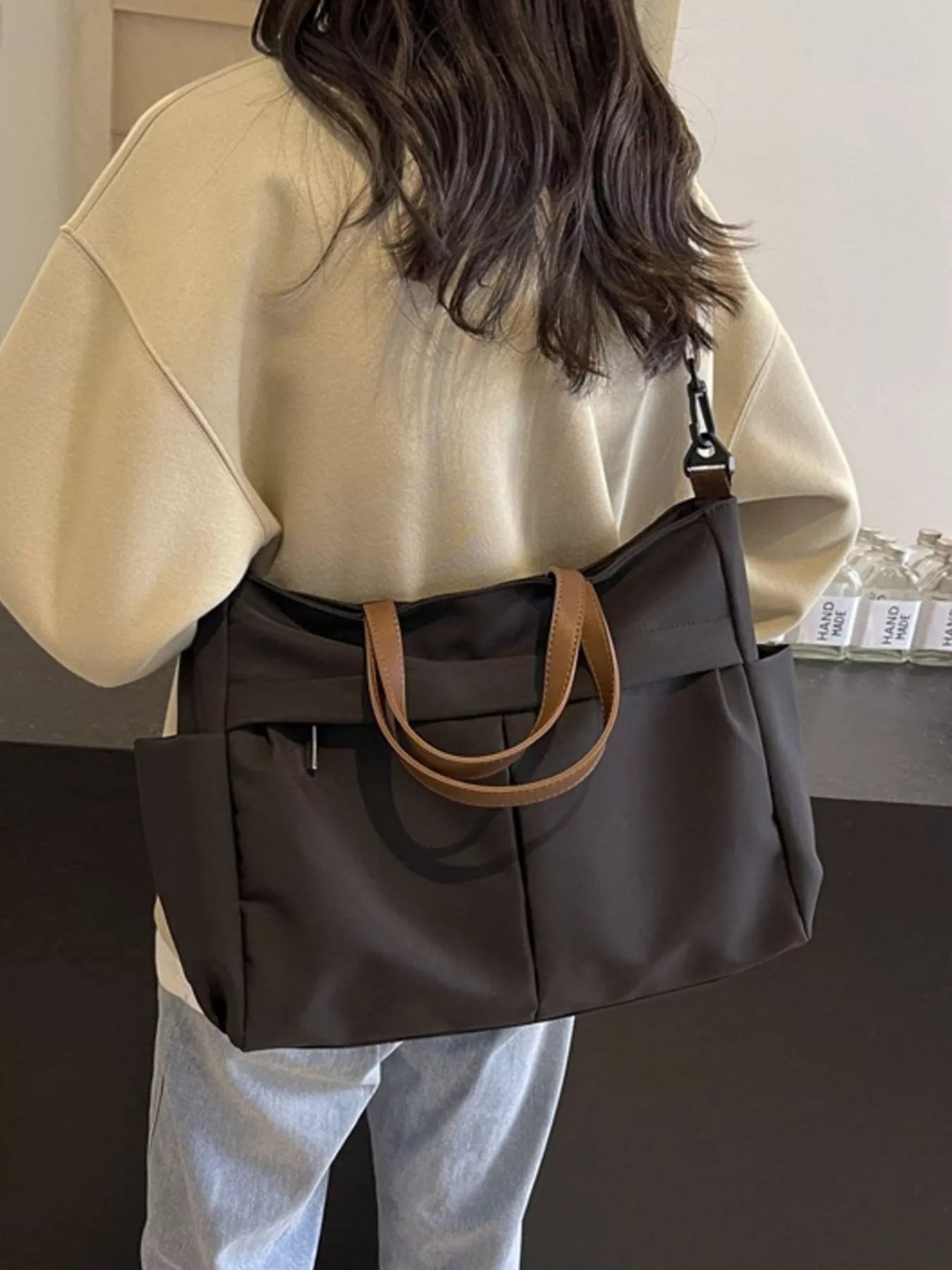 Person wearing a beige top and holding a dark brown handbag with a tan handle.