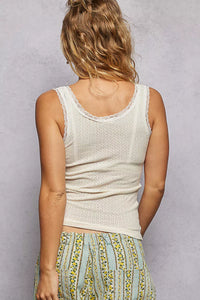 Person wearing a textured beige tank top with floral-patterned pants against a plain background