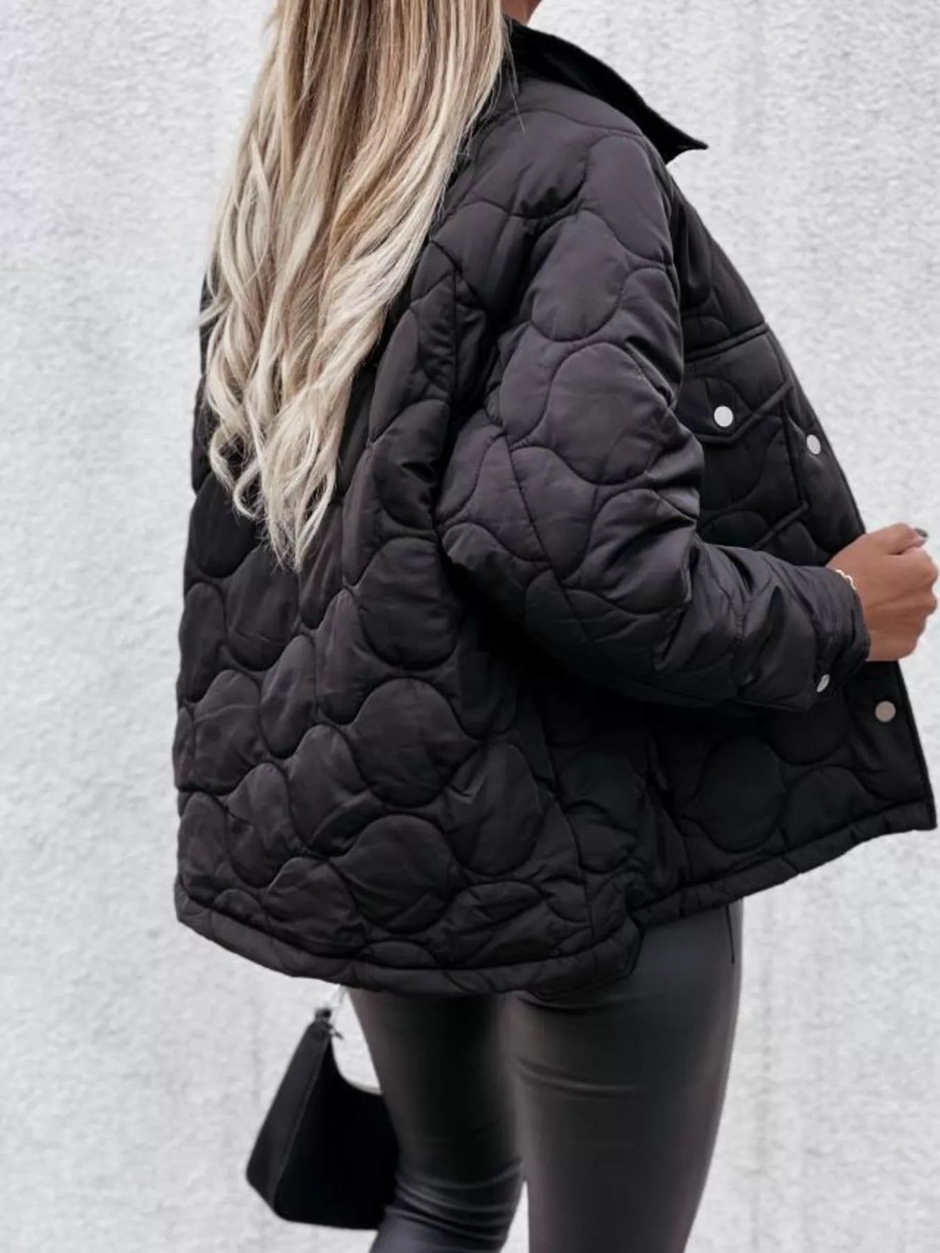 Person wearing a black quilted jacket against a light gray background