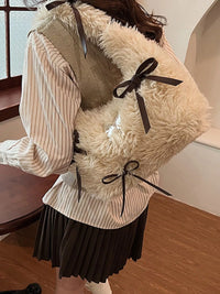 Person wearing a fluffy beige vest with black ribbons indoors.