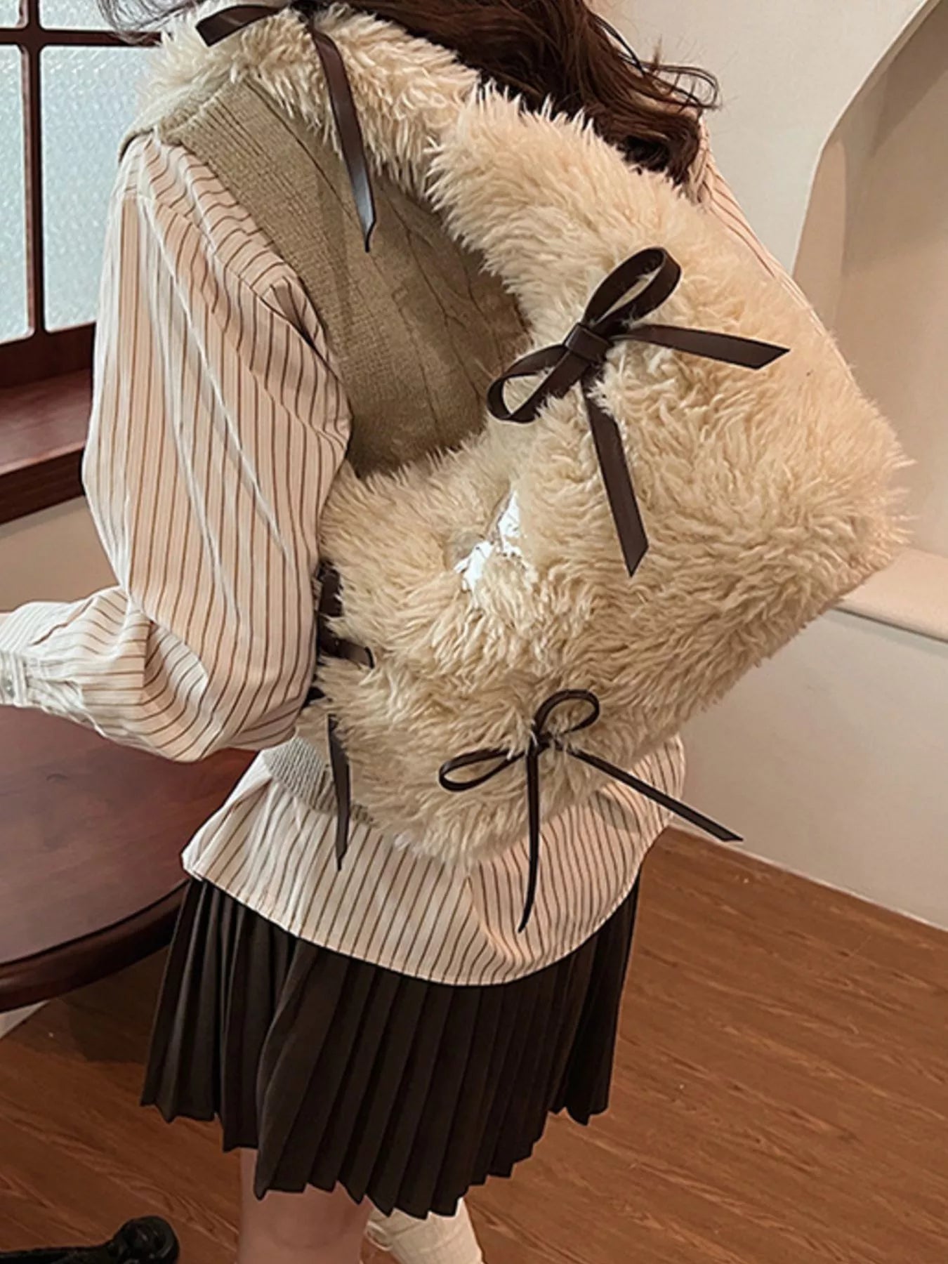 Person wearing a fluffy beige vest with black ribbons indoors.