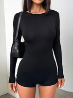 Person wearing a black long-sleeve romper with a plain background