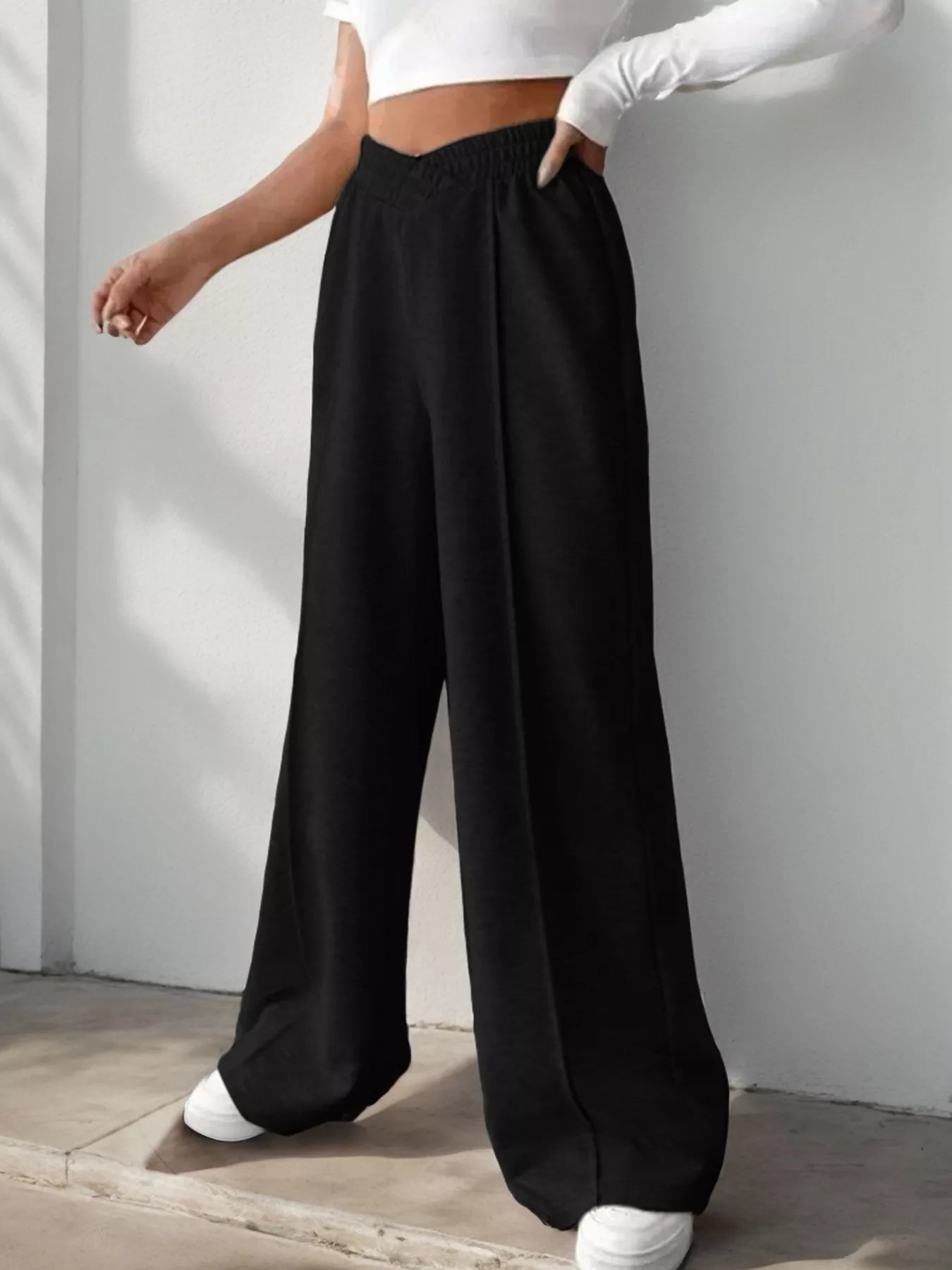 Person wearing black wide-leg pants and a white top against a plain background