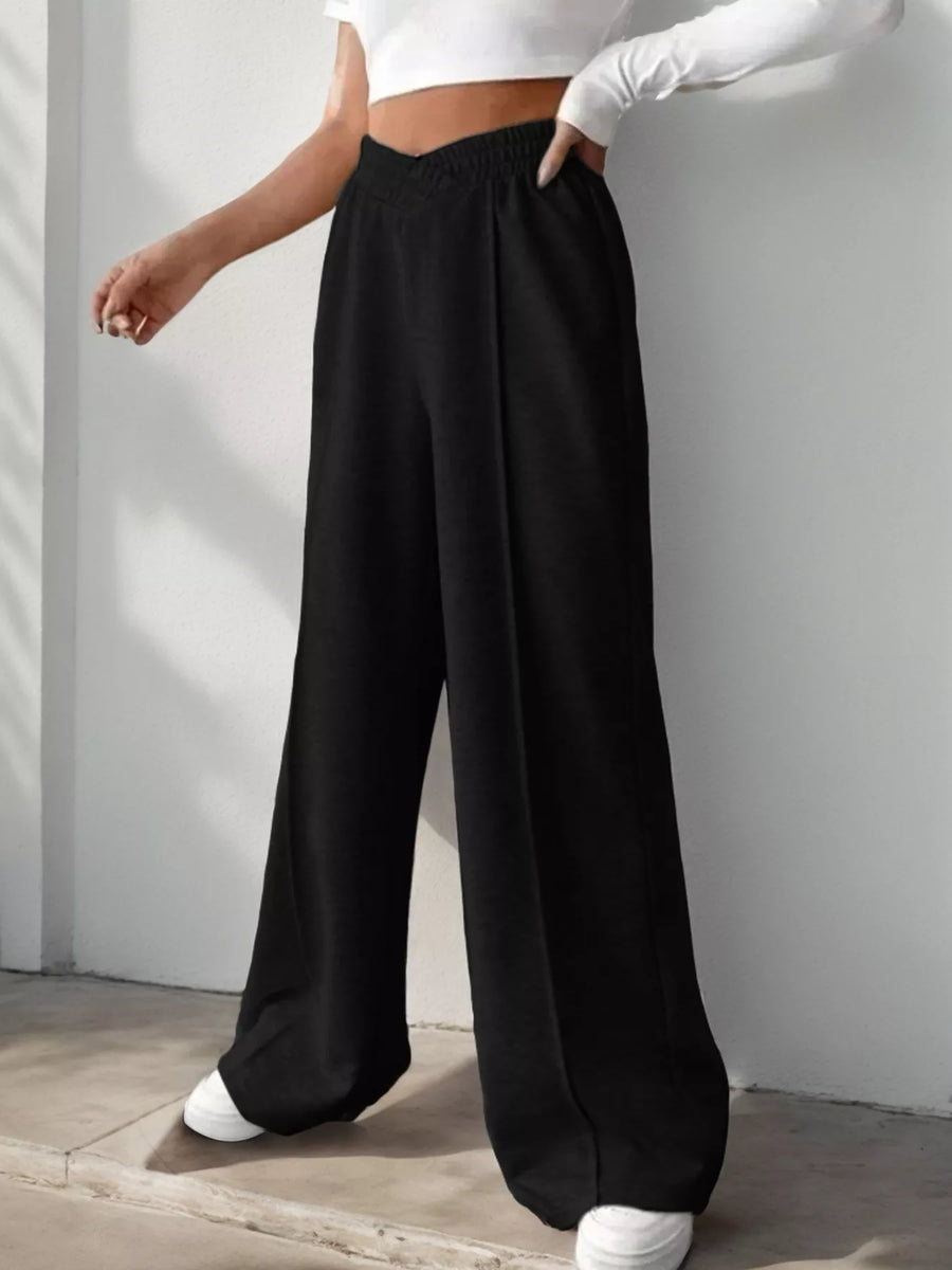 Person wearing black wide-leg pants and a white top against a plain background