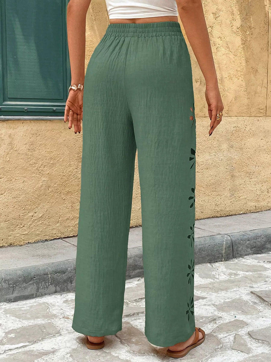 Person wearing green pants with floral patterns walking on a stone pavement.
