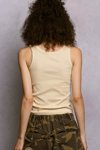 Person wearing a beige tank top and camouflage pants against a gray background