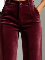 A close-up of a person wearing high-waisted burgundy velvet pants, showing the front waistband, button, fly, and front pockets.