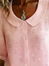 Close-up of a pink blouse with floral patterns and a necklace.