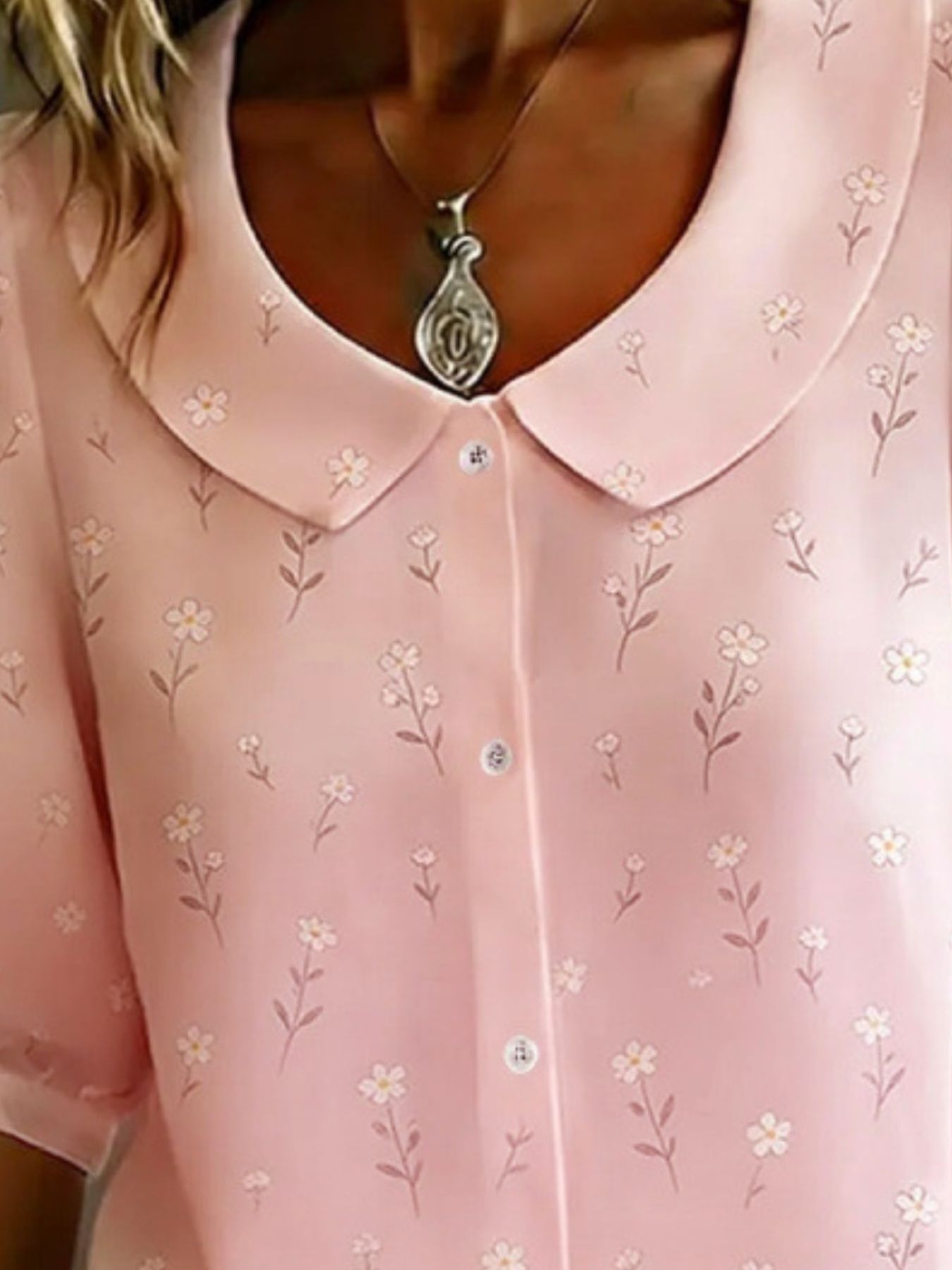 Close-up of a pink blouse with floral patterns and a necklace.