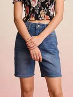 Person wearing a floral top and denim shorts on a beige background